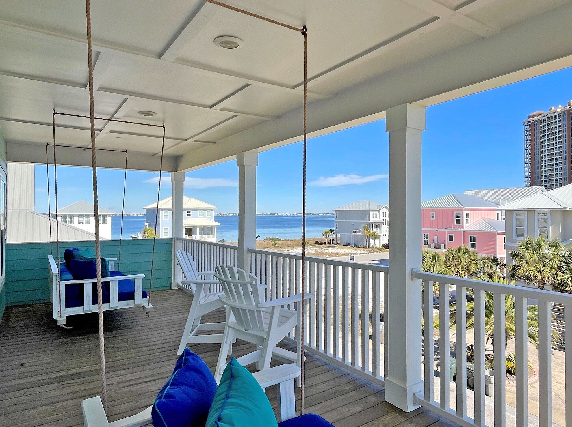 A covered porch with white railings, a swing chair, and a seating area with blue cushions.