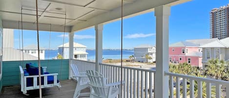 A covered porch with white railings, a swing chair, and a seating area with blue cushions.