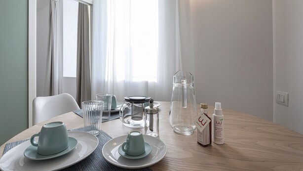 Un comedor con una mesa lista para dos personas, con platos, tazas y una jarra de vidrio.