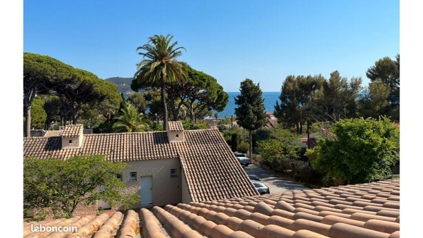 Um edifício em estilo mediterrâneo, com telhas de barro, rodeado por vegetação exuberante e um céu azul límpido.