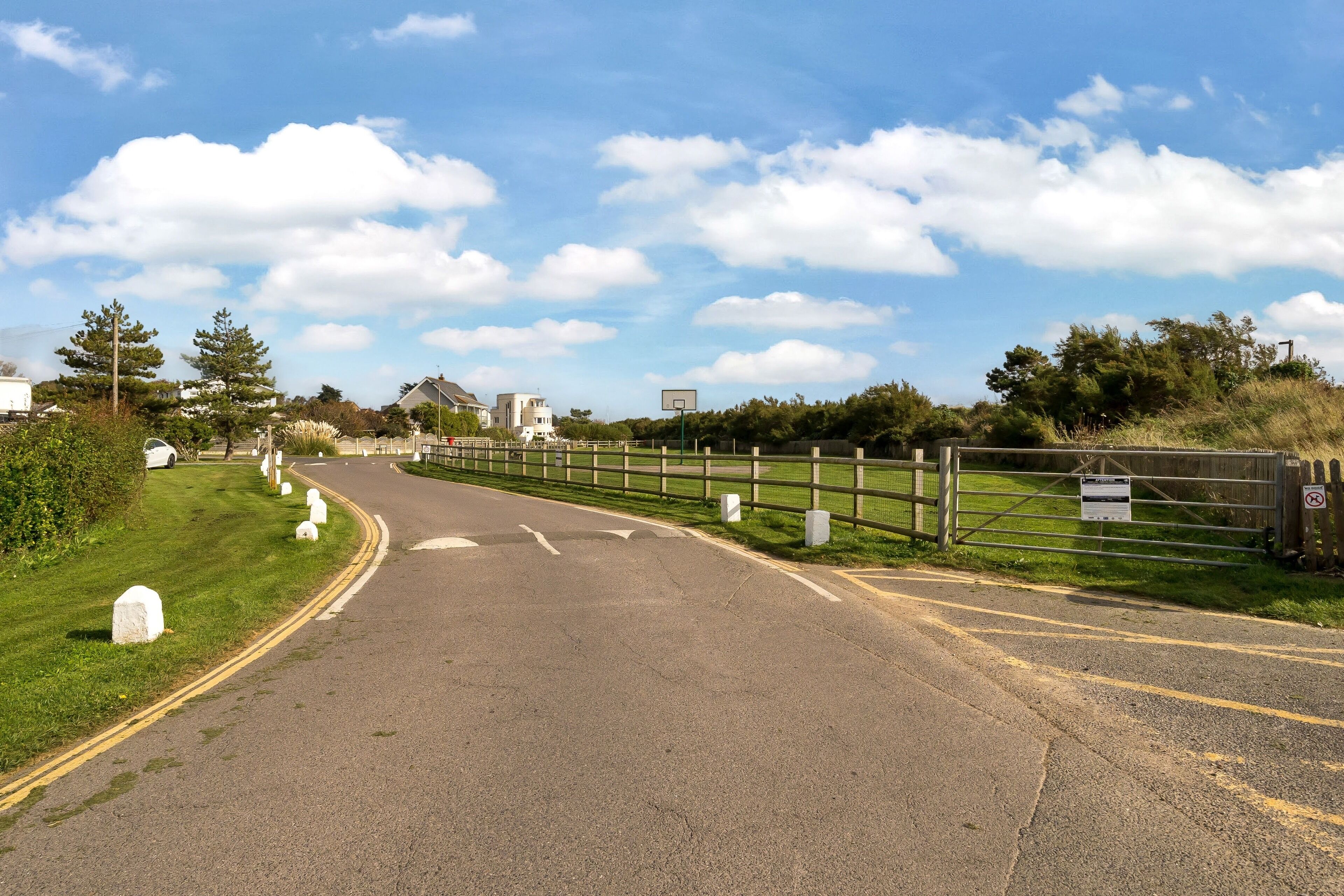 Une route menant à une zone délimitée par des barrières et des potelets blancs, avec un panier de basket et un panneau indiquant qu’il est interdit de se garer.