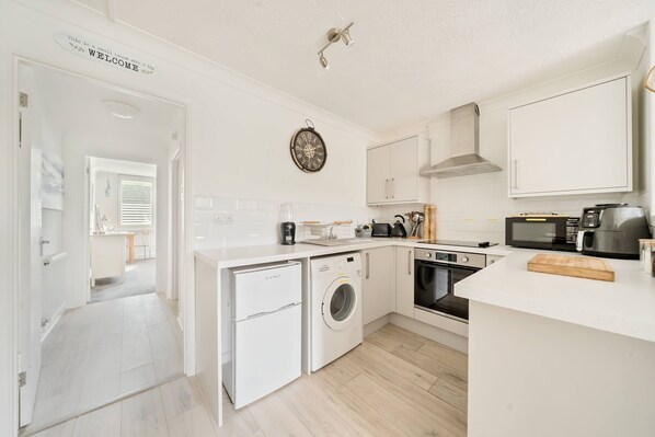 A compact kitchen with a washing machine, oven, microwave, and a clock on the wall.
