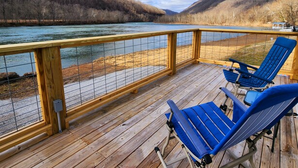 Eine Holzterrasse mit zwei blauen Liegestühlen mit Blick auf einen Fluss und Hügel.