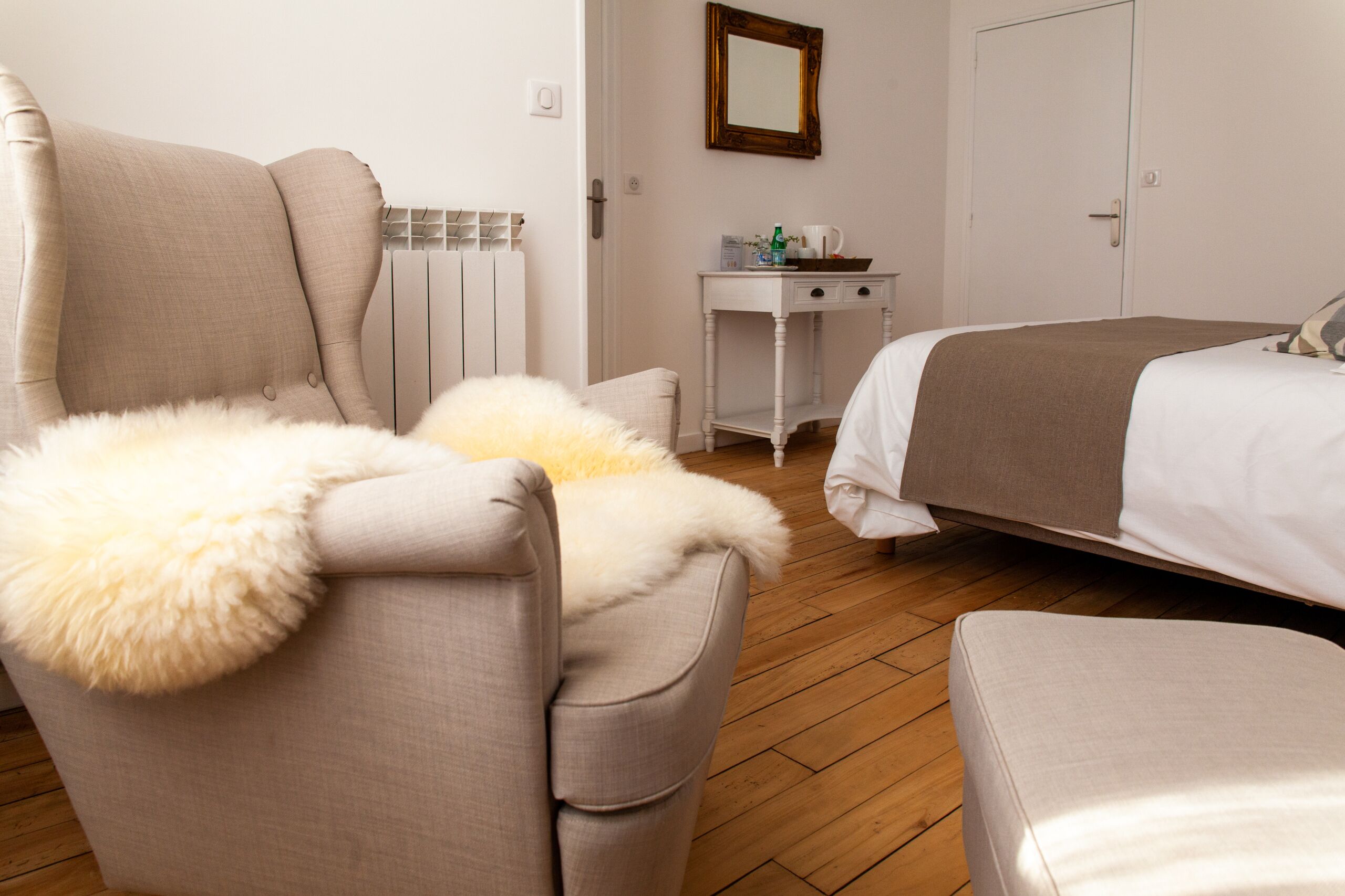Une chambre à coucher avec un lit, une chaise dotée d’un coussin moelleux, une petite table avec un miroir et un radiateur.