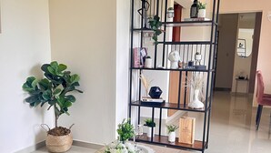 Ein Holztisch mit einer Vase weißer Blumen, einer Topfpflanze und einem Bücherregal mit dekorativen Gegenständen.