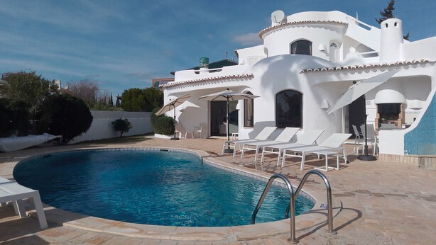 En modern, vit villa med en swimmingpool, utomhusmöbler och en grillplats.