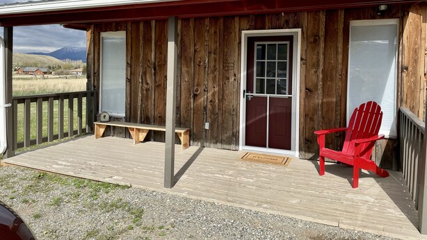 A wooden building with a porch, a red chair, and a welcome mat. - Cozy cottage nestled in Paradise Valley surrounded by mountain views! (Livingston)