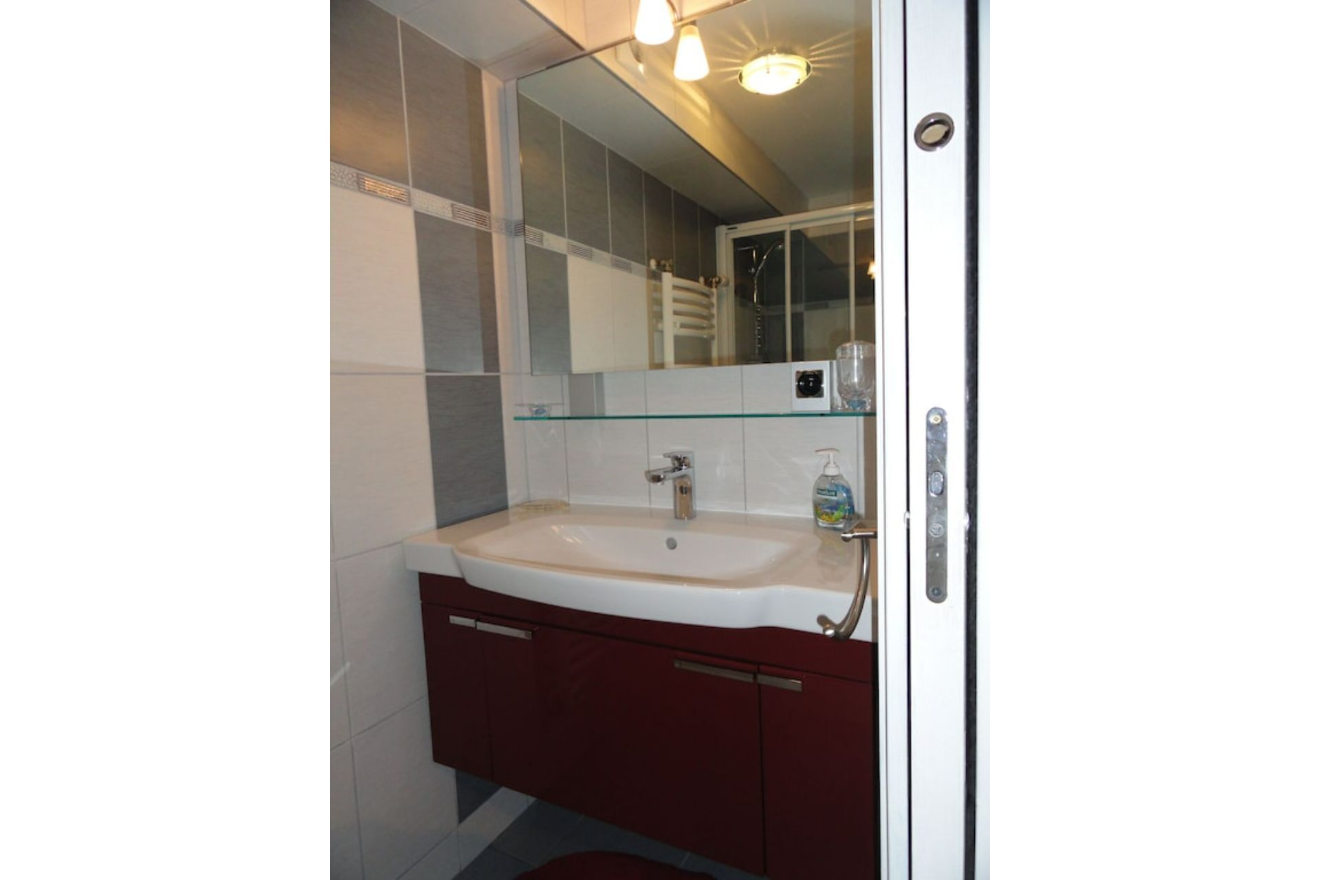 A bathroom with a white sink, a glass shelf, and a mirror above the sink.