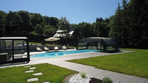Un patio trasero con piscina, sillas de descanso y un área de patio con cerramiento de vidrio.