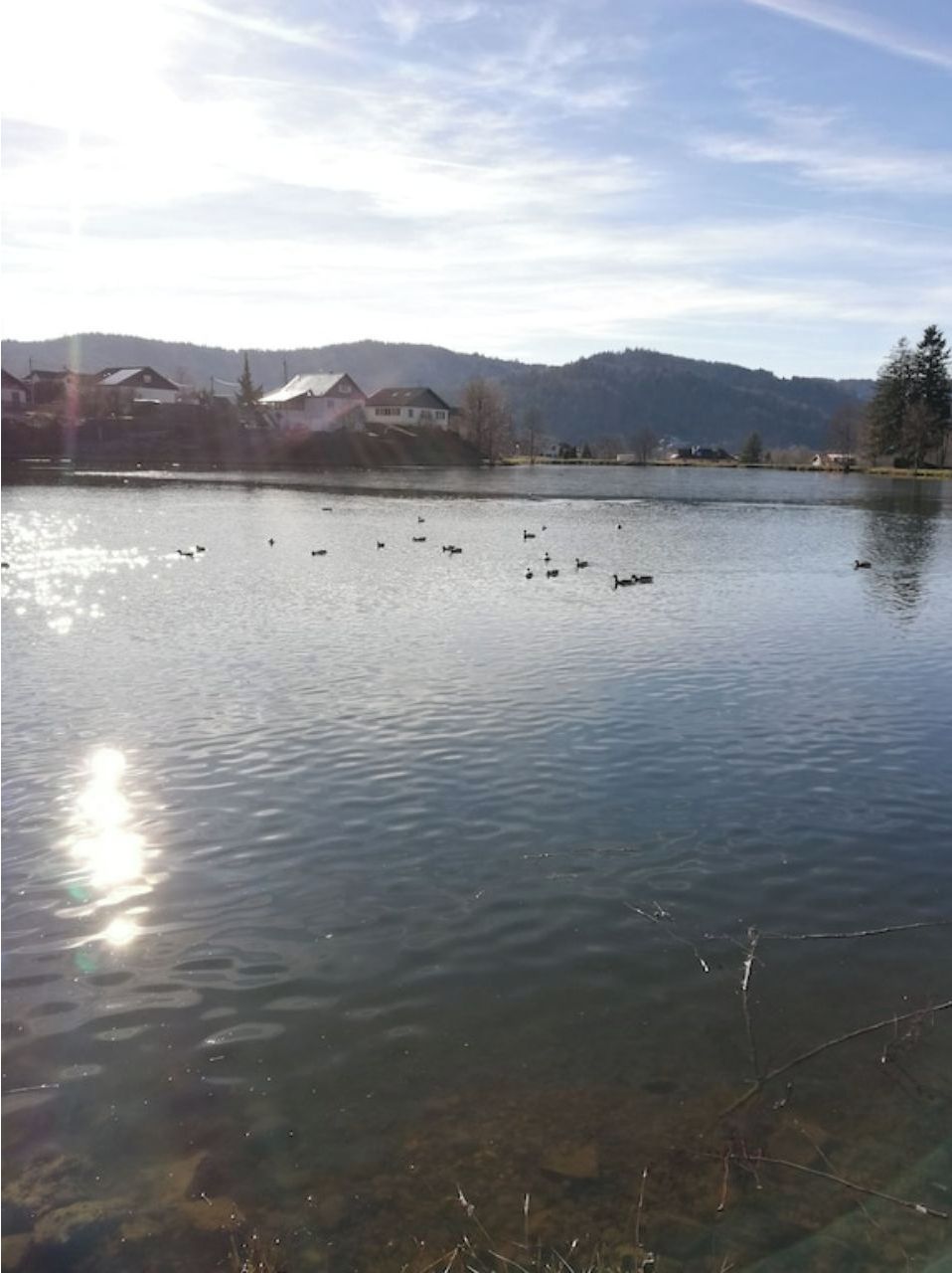 A lake with clear water, surrounded by houses and hills in the background.