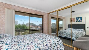 A hotel room with a large bed, a chair, a mirror, and a view of the outside.