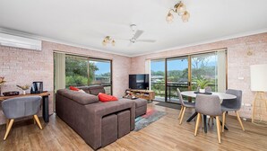 A modern living room with a brown sectional sofa, a TV, and a dining area with a table and chairs.