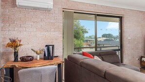 A modern living room with a brick wall, a large sliding glass door, a grey sofa, a wooden table with decorative items, and a small side table.