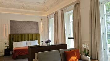 A hotel room with a bed, a sofa, a dining table with glasses and a vase, and a large painting on the ceiling.