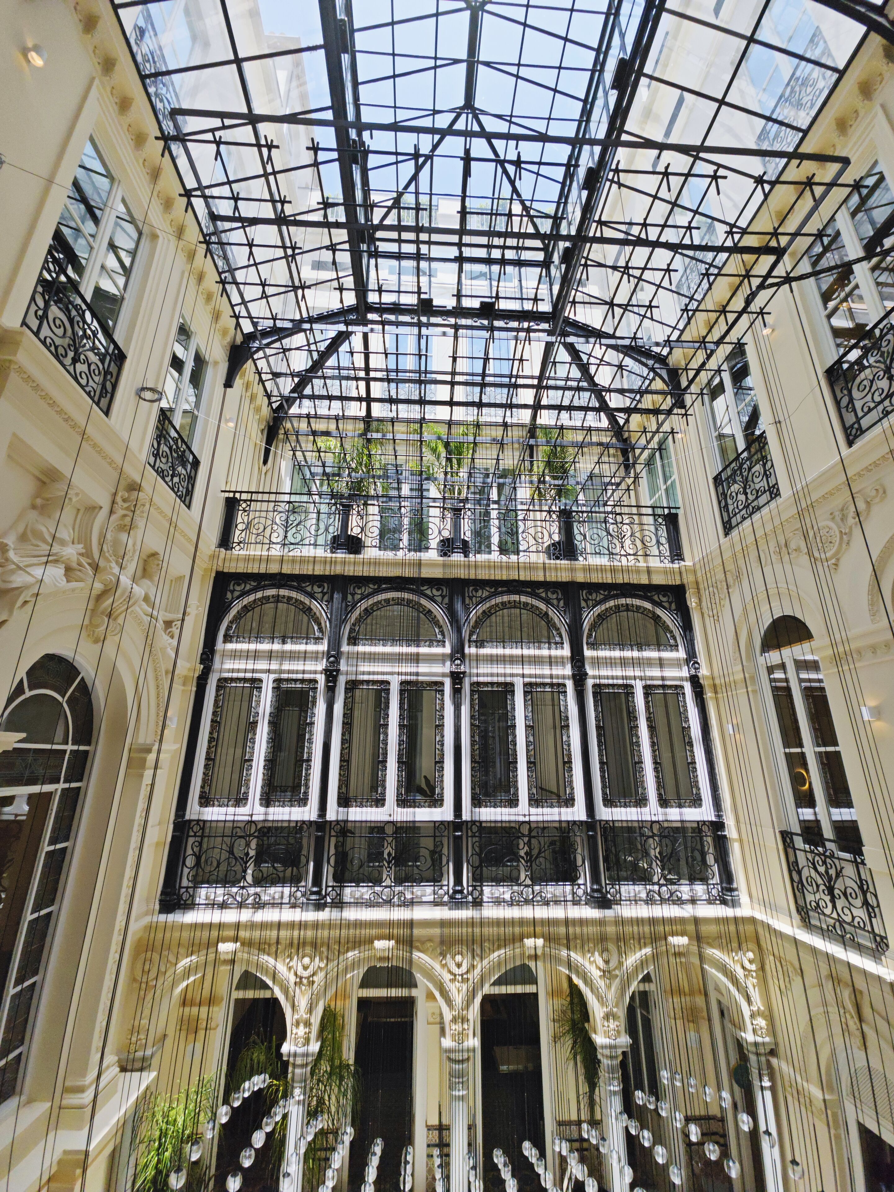Un vaste atrium doté d’un plafond en verre, de balustrades en fer forgé ouvragées et d’une architecture de style classique.