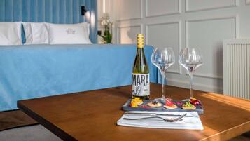 Habitación de hotel con cama, una mesa de madera con una botella de vino, dos copas y una bandeja con comida.