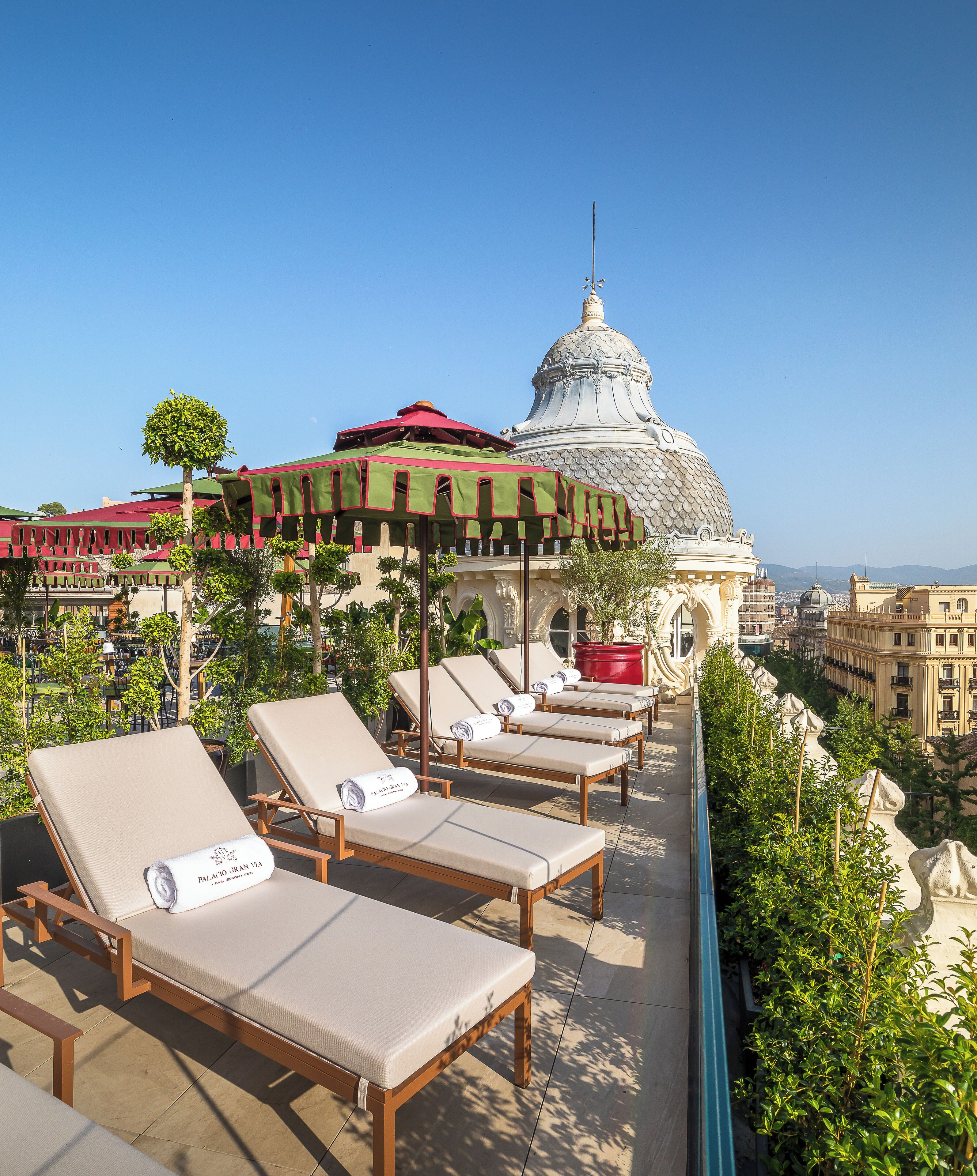 Área de estar no terraço com espreguiçadeiras e um espaço coberto para sentar, com vista para um horizonte urbano com edifícios em cúpula.