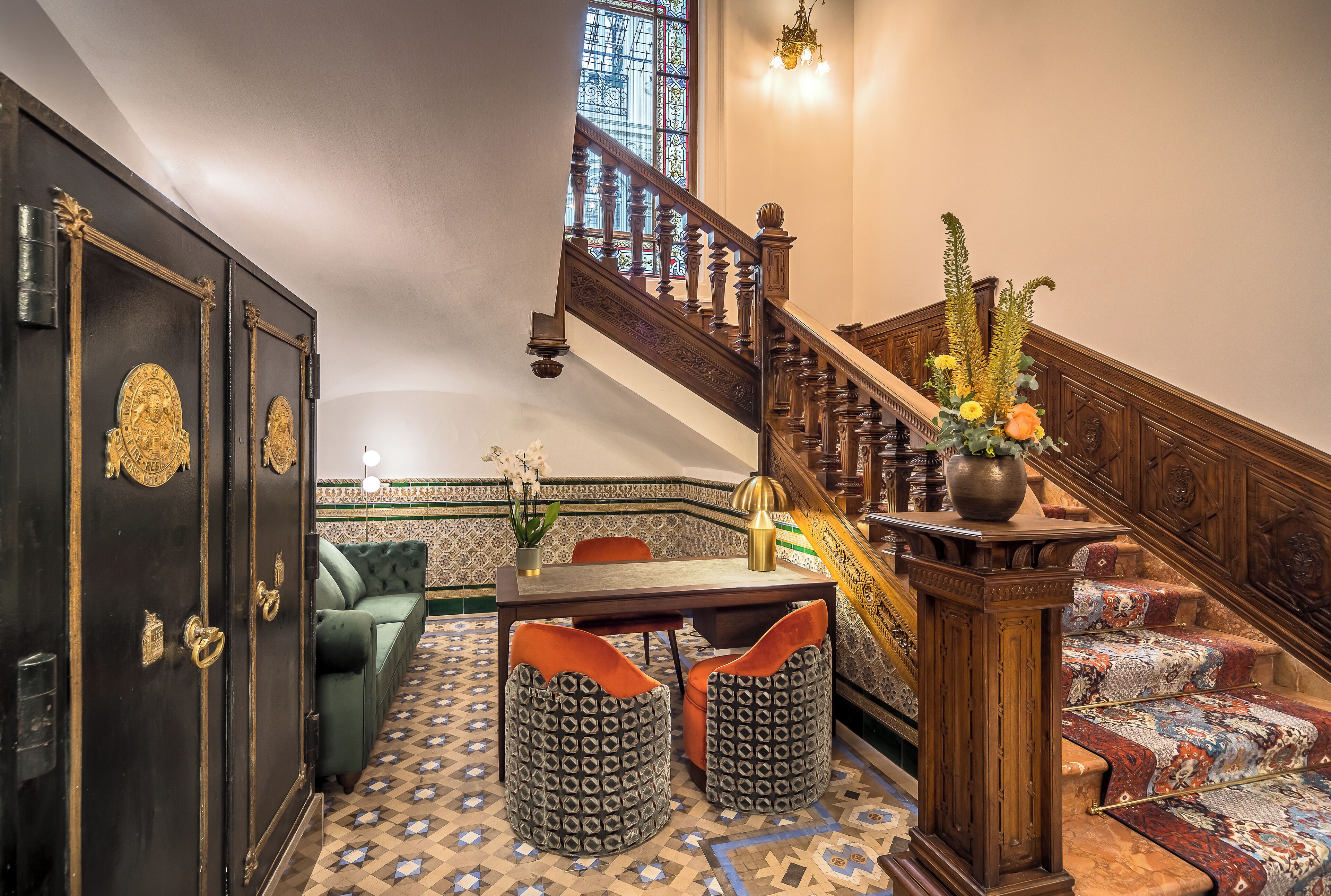 Eine Treppe mit aufwendiger Holzvertäfelung, ein grünes Sofa, gemusterte Hocker und ein Esstisch mit Stühlen.