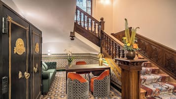 Una escalera con detalles de madera decorativos, un sofá verde, otomanas estampadas y una mesa de comedor con sillas.