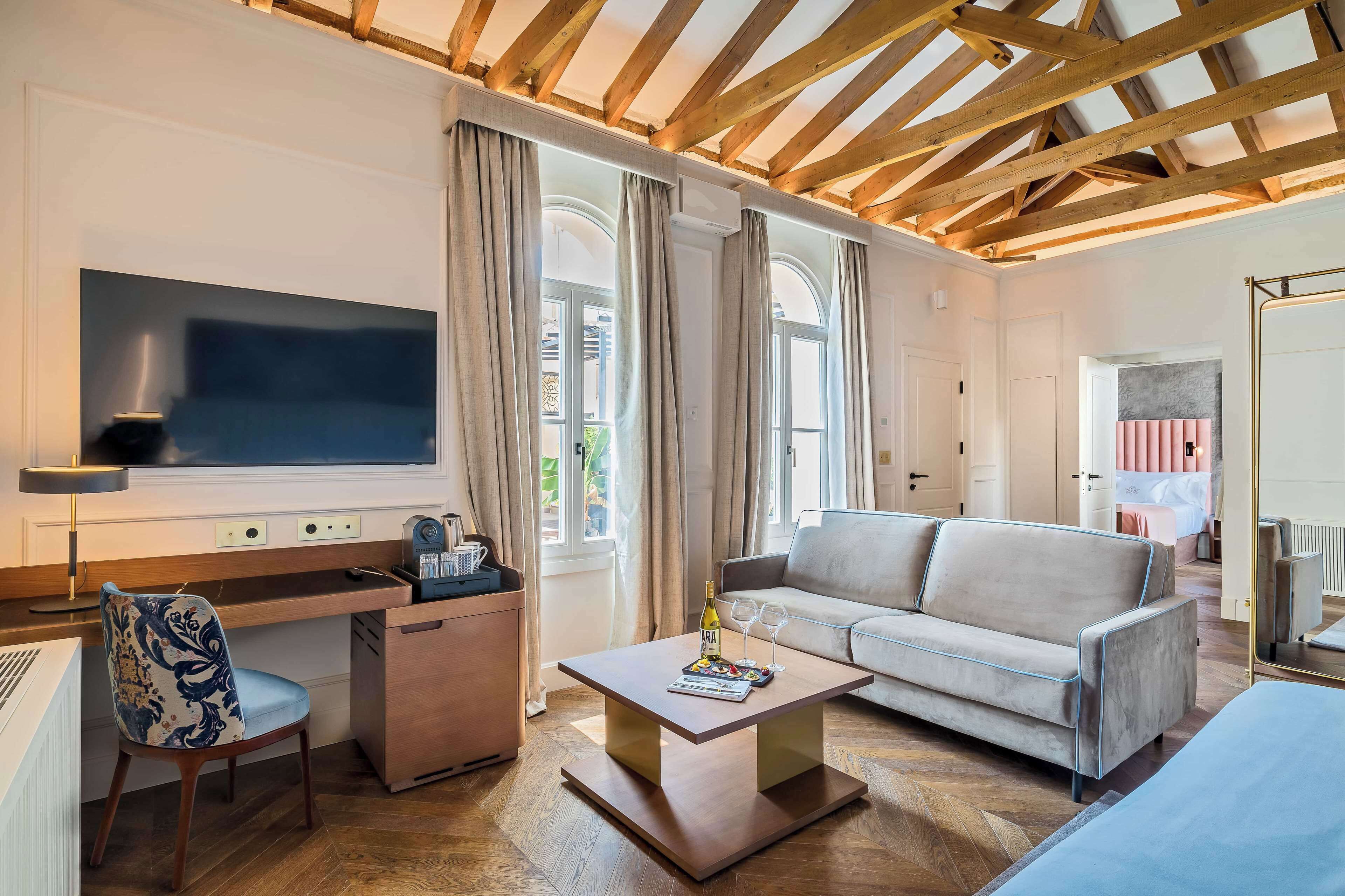 A modern living room with a wooden ceiling, a flat-screen TV, a sofa, a coffee table, and a desk with a chair.