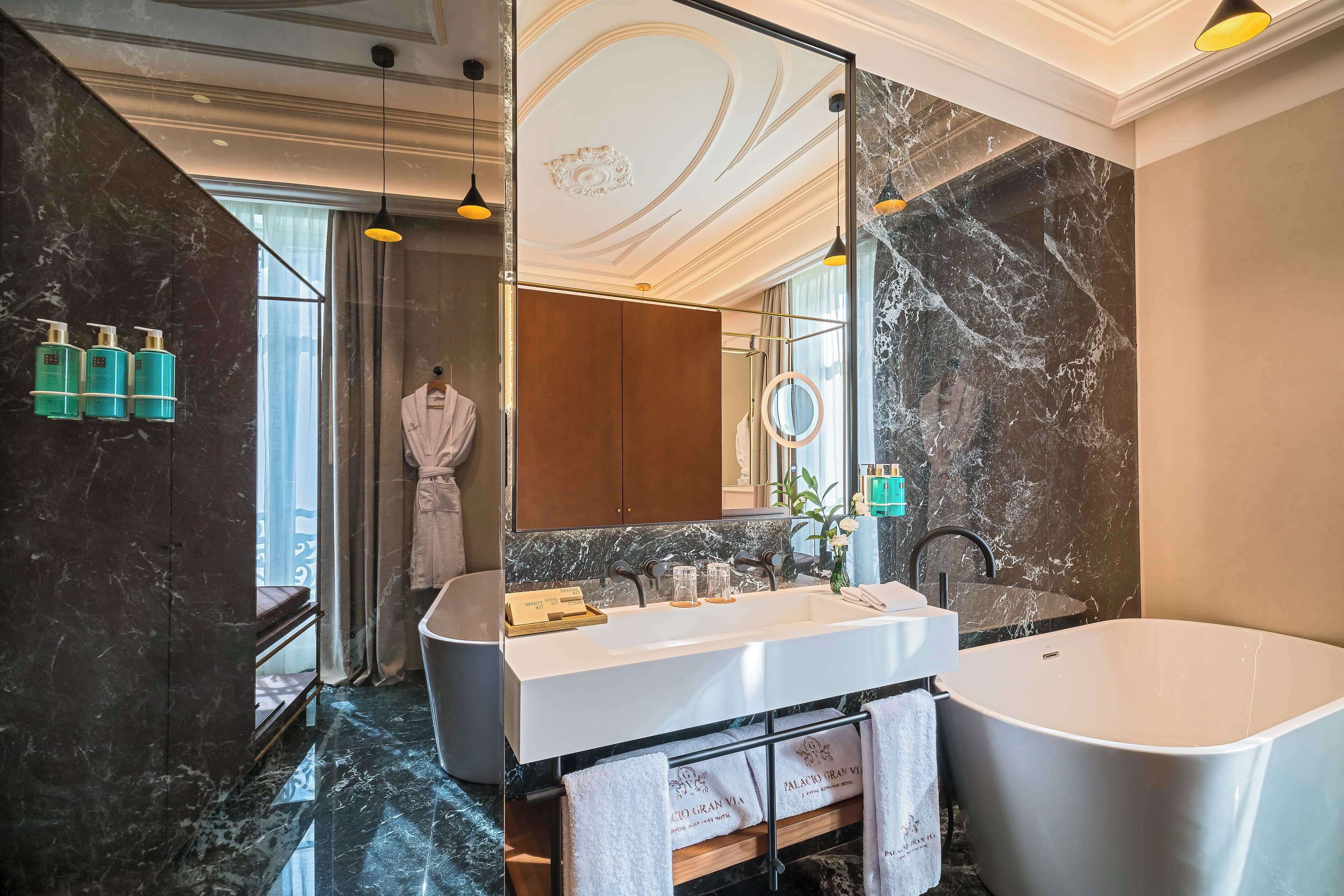 A modern bathroom with a large bathtub, a vanity with a mirror, and marble walls.