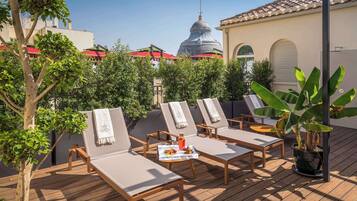 Terraza en la azotea con sillones de descanso, una mesa con bebidas y aperitivos, y vistas a un edificio con cúpula y tejados rojos.