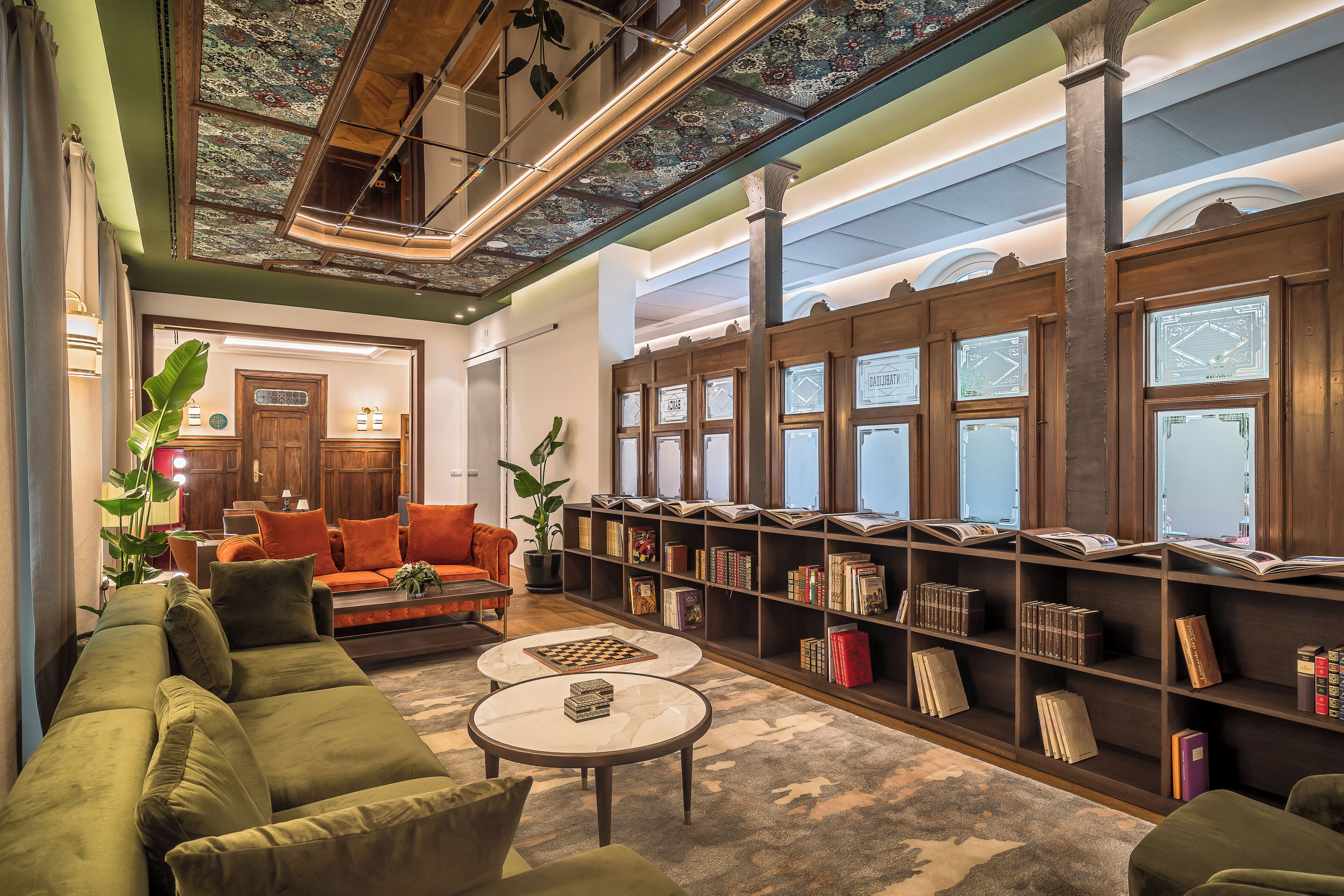 Et bibliotek med bogreoler, en grøn sofa og et skakspil.