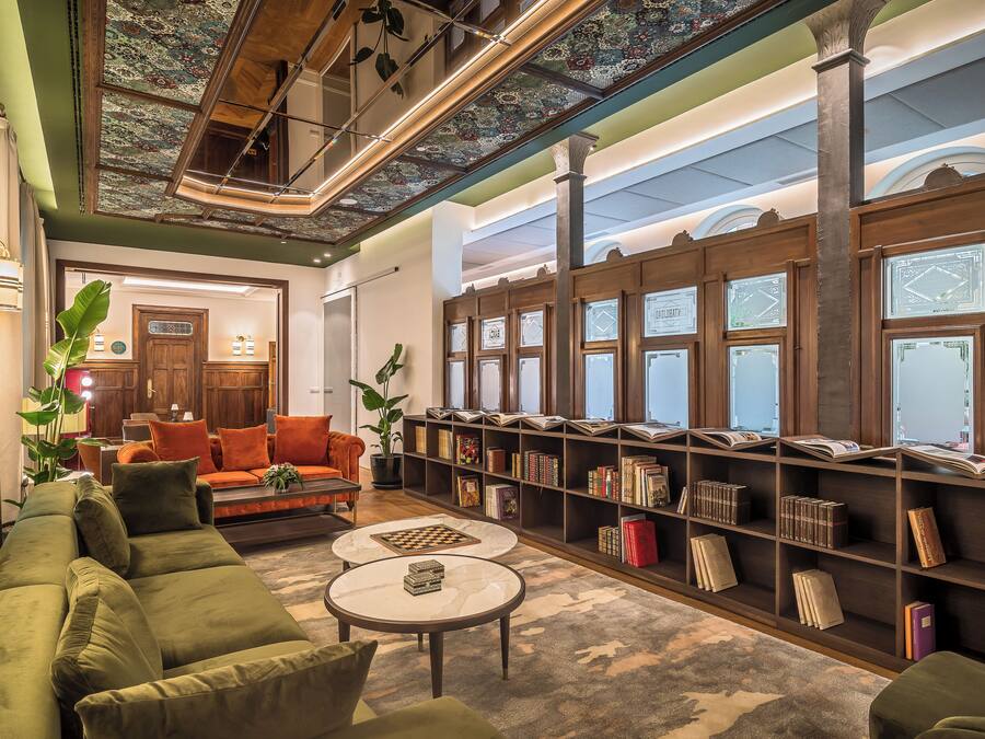 Et bibliotek med bogreoler, en grøn sofa og et skakspil.