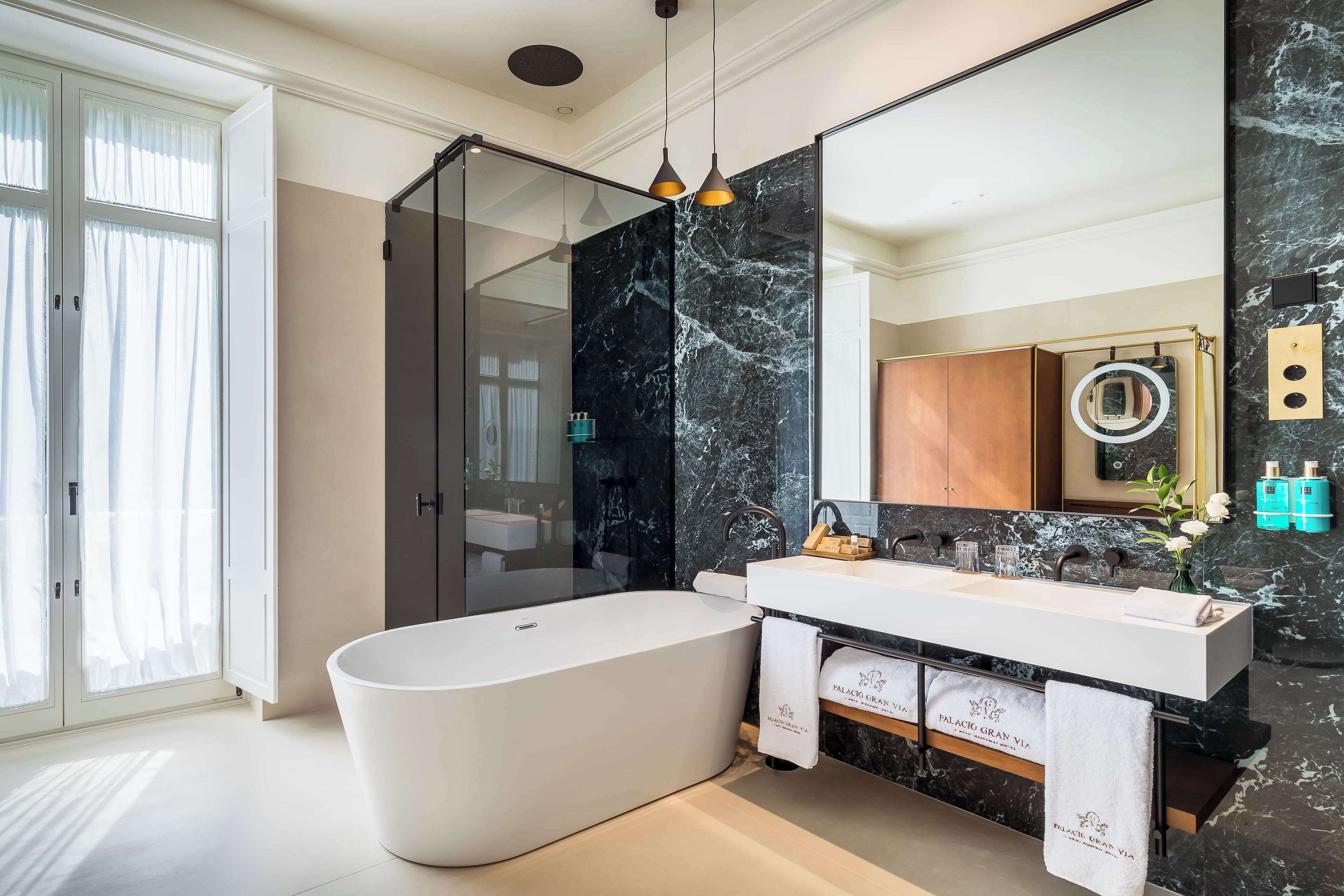 A modern bathroom with a freestanding bathtub, a large mirror, and a marble backsplash.