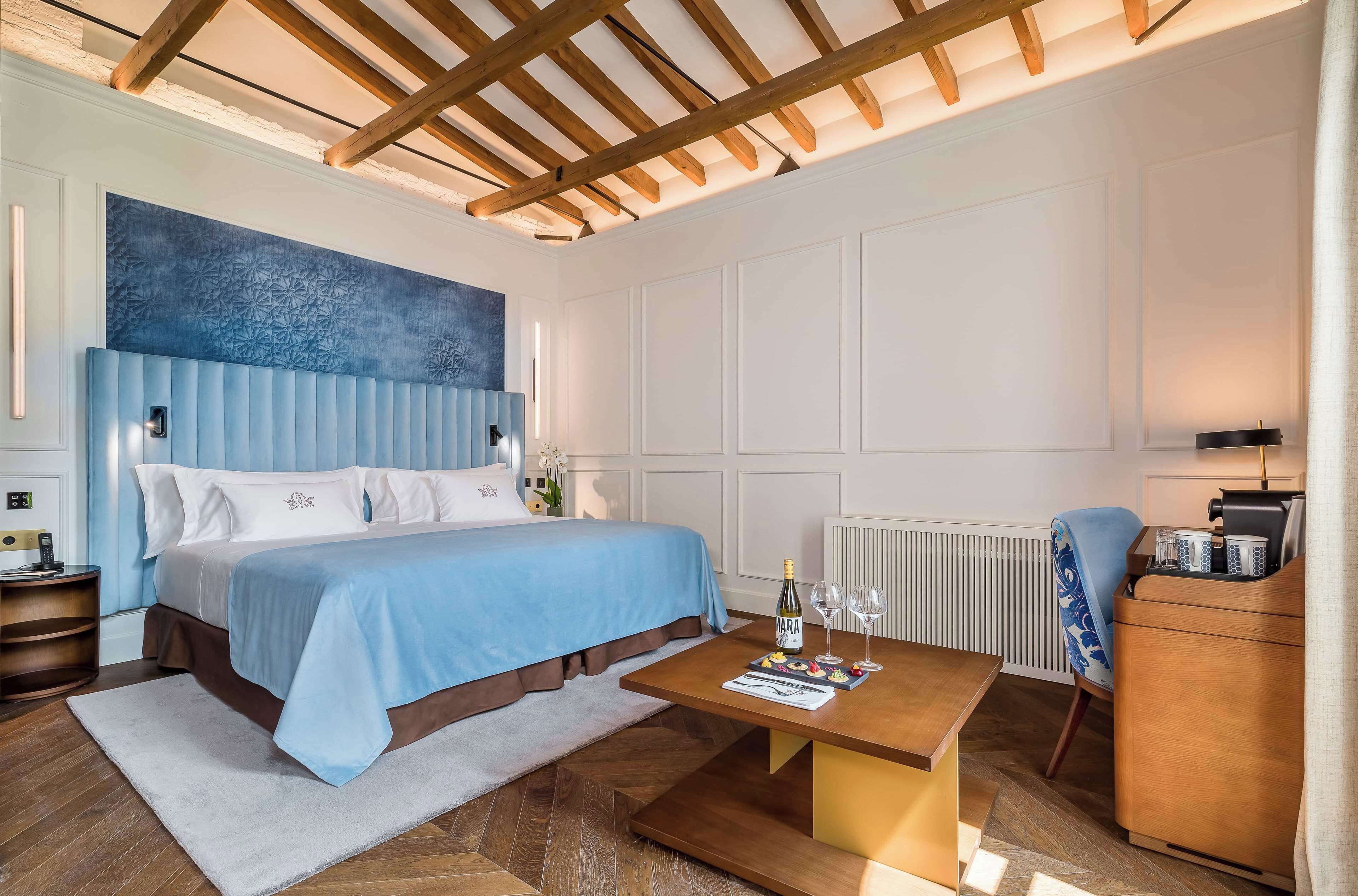 Une chambre d’hôtel moderne avec un grand lit, une table basse en bois, une table de chevet et une commode.