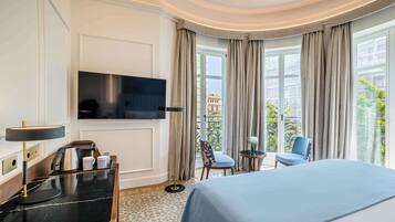 Ein Hotelzimmer mit Bett, Schreibtisch mit Lampe, Fernseher und Blick auf die Stadt durch große Fenster.