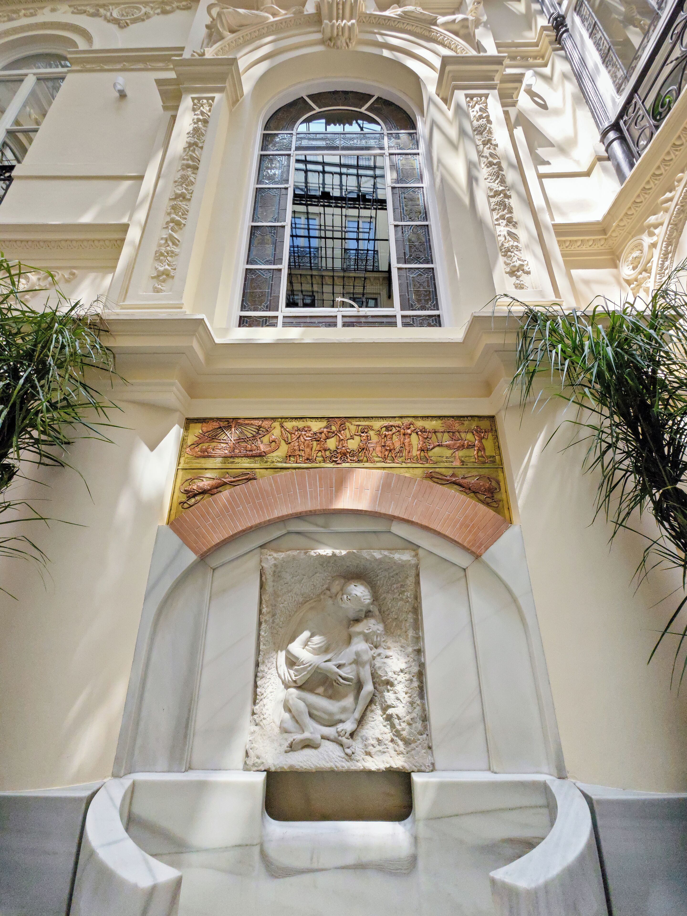 An ornate architectural detail with a relief sculpture of a figure, a window with intricate iron bars, and a decorative tiled archway.