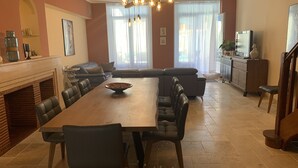 A spacious dining area with a long table, multiple chairs, a fireplace, and a modern kitchen in the background. - Logis de la Foulerie (Bize-Minervois)