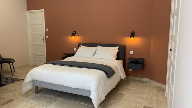 A bedroom with a bed, two bedside tables, a chair, and a door. - Logis de la Foulerie (Bize-Minervois)