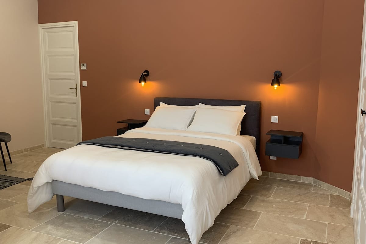 Ein Schlafzimmer mit einem Bett, zwei Nachttischen, einem Sessel und einer Tür.