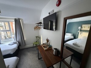 A hotel room with two single beds, a wooden table with a kettle, a chair, a TV mounted on the wall, and a window with curtains. - Old Ship Inn (Dorchester)