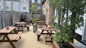 An outdoor patio area with multiple wooden picnic tables and benches, surrounded by a wooden fence. - Old Ship Inn (Dorchester)
