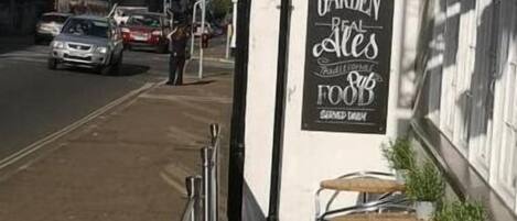 Une vue d’une rue, avec un bâtiment sur lequel on peut voir une enseigne indiquant « Beer Garden Real Ales » et une autre enseigne, « ACCOMM », au-dessus d’une porte.