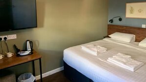 A neatly made bed with white linens, a bedside table with a coffee maker, and a flat-screen TV mounted on the wall. - Old Ship Inn (Dorchester)