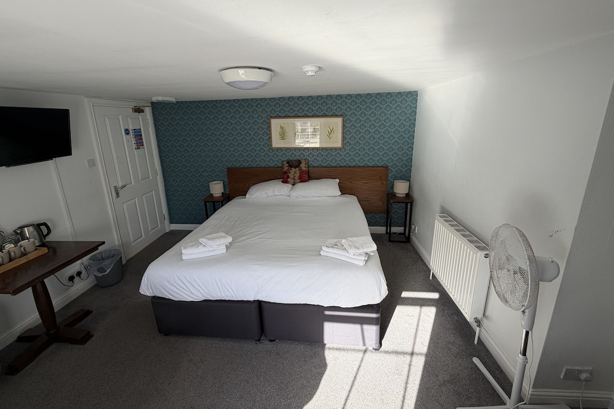 A neatly arranged bedroom with a bed, bedside tables, a TV, and a radiator.