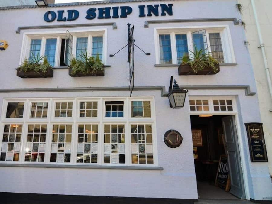 The exterior of the Old Ship Inn, featuring a traditional facade with multiple windows, a prominent sign, and hanging plants.