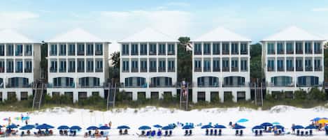 A beachfront hotel with multiple balconies, a sandy beach, and several umbrellas.