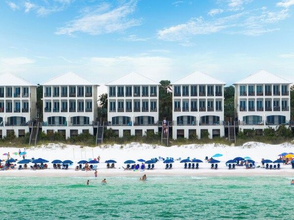 Un hotel frente a la playa con varios balcones y una zona de playa con sombrillas.
