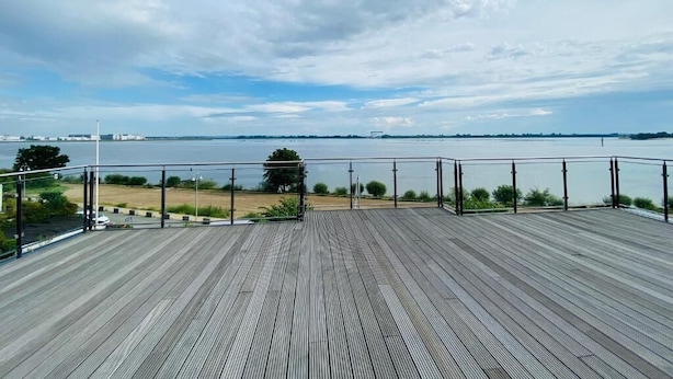 A wooden deck with a metal railing overlooking a body of water and distant land. - Homaris Strandhaus Blankenese (Hamburg)