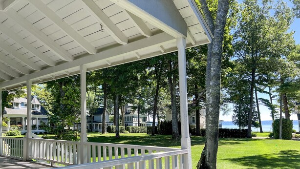 A covered porch with white railings, a grassy lawn, and houses in the background.