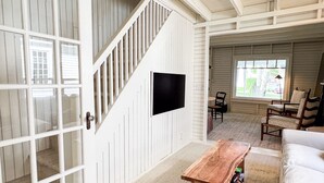A spacious living area with a staircase, a flat-screen TV mounted on the wall, and a cozy seating arrangement with a sofa and chairs.