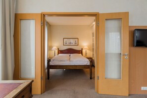 Une chambre d’hôtel avec un lit, deux lampes de chevet, un téléviseur fixé au mur et une porte donnant sur une autre pièce.