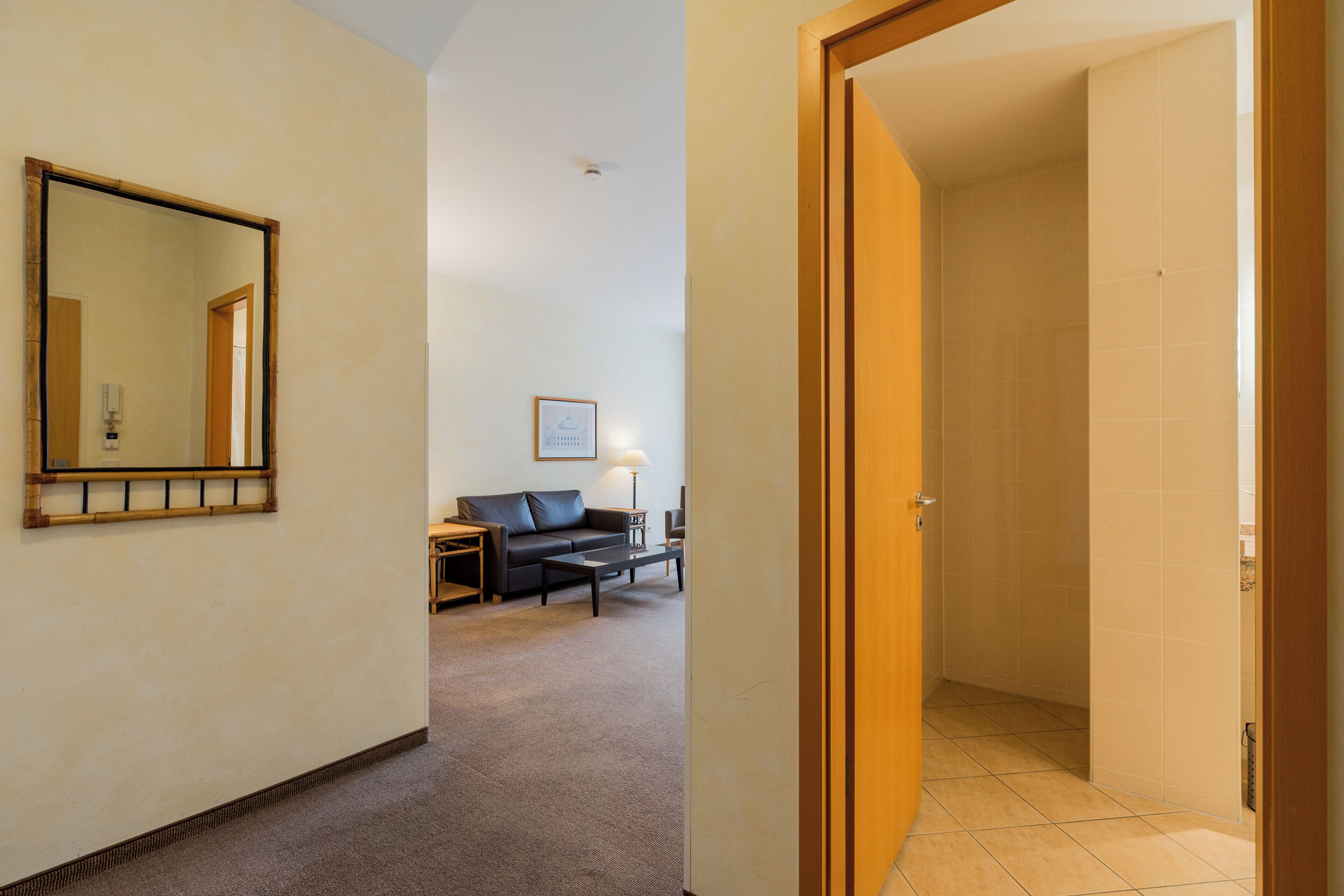 Quarto de hotel com um espelho grande, um sofá, uma mesa de centro e um abajur.