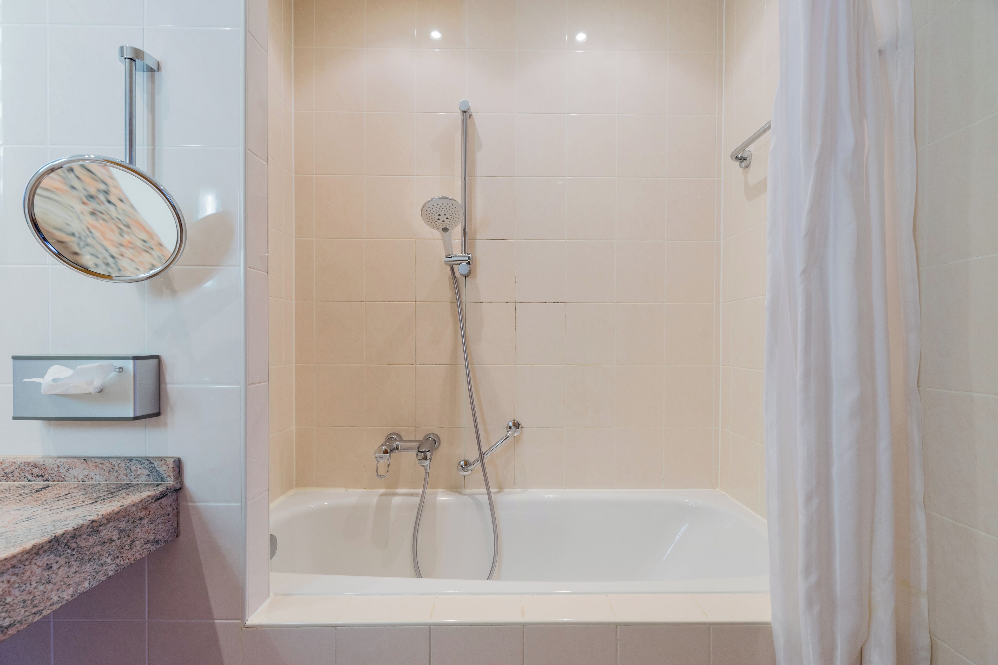Un baño con bañera, cabezal de ducha, toallero y espejo.