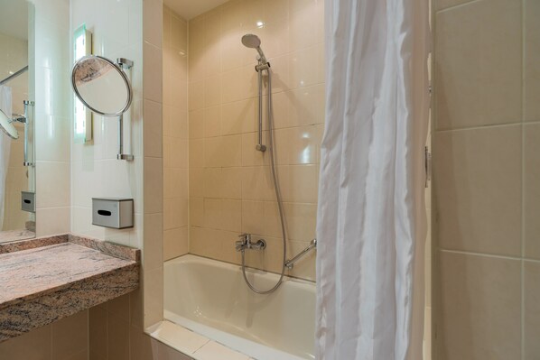 A bathroom with a granite countertop, a bathtub, a shower with a handheld showerhead, and a wall-mounted mirror. - Apartmenthaus Berlin Mitte (Berlin)